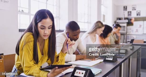 教室でタブレットを読んでいる女性、大学の仕事とテクノロジーによる教育の革新を学ぶ学生。机上での学校グループライティング、インターネットによる大学研究、研究奨学金 - economics college ストックフォトと画像