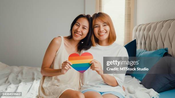 young beautiful asia lesbian couple ladies in bedroom. happy girls smile looking at camera show rainbow heart lgbt community symbol together on bed at home. - equality logo stock pictures, royalty-free photos & images