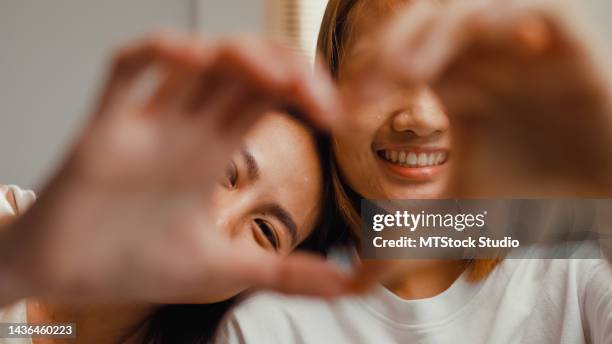 close-up young romantic asian female lesbian in bedroom. happy girls making fingers heart shaped signs on bed. - happy face close up stockfoto's en -beelden