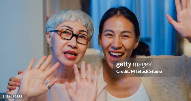 happy asian family, young daughter and senior elderly mom looking at camera teach older mother to use video call online to friends spend time in home weekend at night. - mother daughter webcam stockfoto's en -beelden