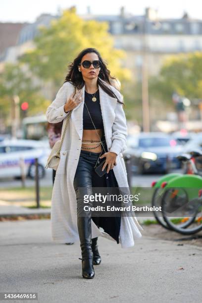 Guest wears black sunglasses from Chanel, gold chain pendant necklace, a black cropped t-shirt, a white tweed long coat from Chanel, a beige shiny...