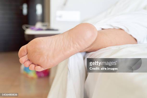 unrecognizable person lying in bed under a white blanket with one foot out of bed - human foot fotografías e imágenes de stock