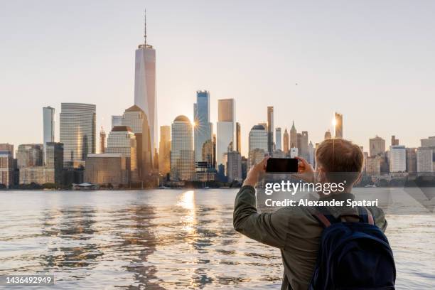 man photographing new york skyline with smartphone, rear view, usa - new york tourist stock-fotos und bilder