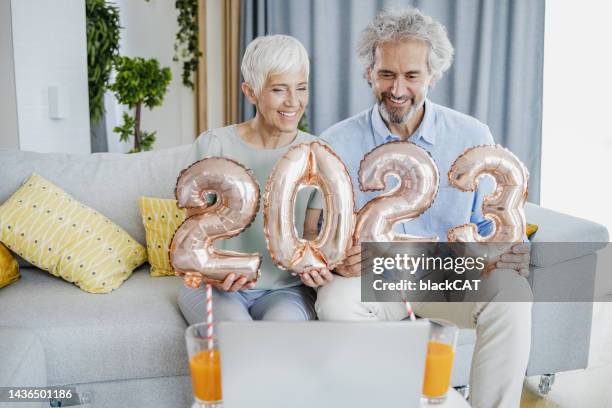seniorenpaar mit ballonnummern als symbol für 2023. jahr und gespräch über einen videoanruf per laptop - 50 year old black woman stock-fotos und bilder