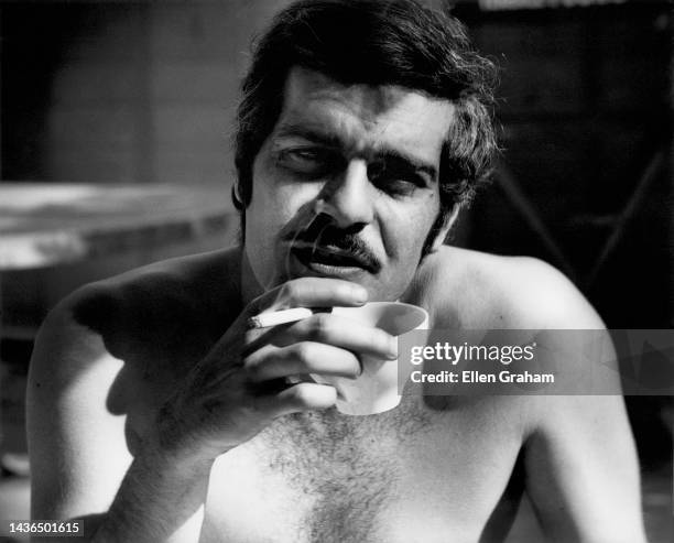 Portrait of Egyptian actor Omar Sharif , shirtless, as he holds a cigarette and coffee cup in one hand, Malibu, California, 1967.