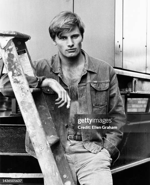 Portrait of American actor Viggo Mortensen, his shirt unbuttoned, as he leans against a ladder, New York, New York, 1983.