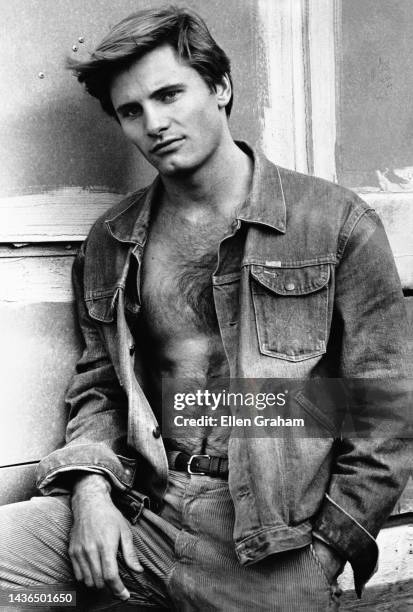 Portrait of American actor Viggo Mortensen, his shirt unbuttoned, as he leans against a window, New York, New York, 1983.