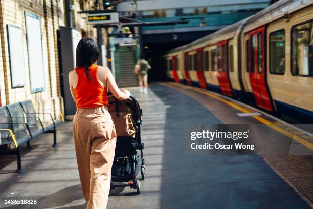 rear view of young mother leaving the train, walking on platform with her baby sitting in pushchair - perron stockfoto's en -beelden
