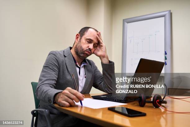 tired businessman looking at laptop while sitting at desk in creative finance office. working concept. - gonzalo caballero fotografías e imágenes de stock