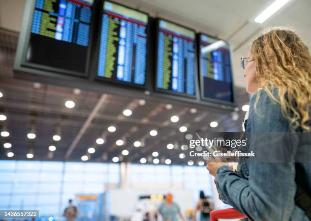 mulher verificando horário de embarque no horário digital no aeroporto - voando - fotografias e filmes do acervo
