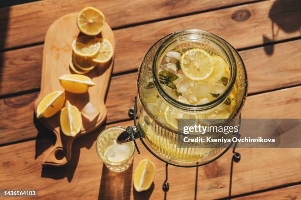 lemonade with ice in a pitcher and glass on a wooden table with fruit and crushed ice outside with a lemon field in the background on a sunny day. front view. horizontal composition. - zitronen feld stock-fotos und bilder
