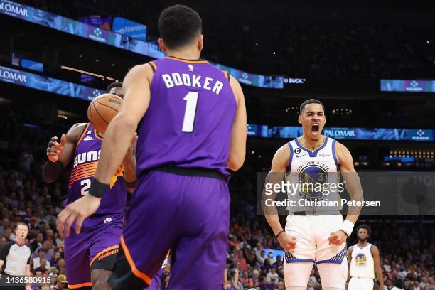 Jordan Poole of the Golden State Warriors reacts after scoring against Deandre Ayton and Devin Booker of the Phoenix Suns during the first half of...