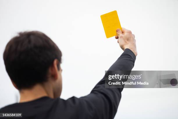 male soccer referee lifting up a yellow card during match - blame game stock pictures, royalty-free photos & images