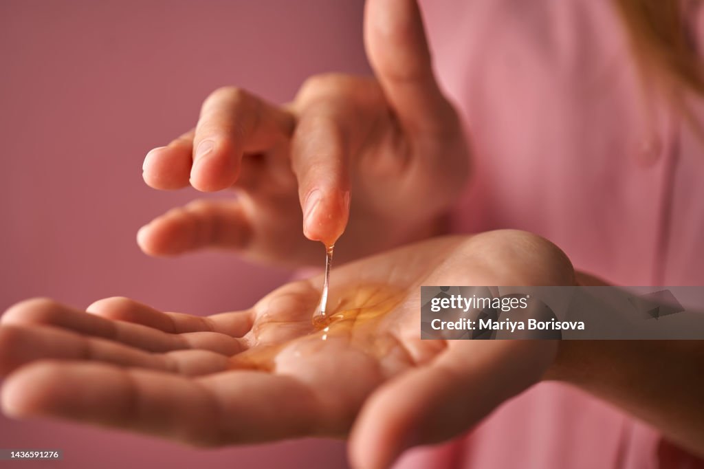 A girl in pink touches a gel cosmetic in her palm with her finger.