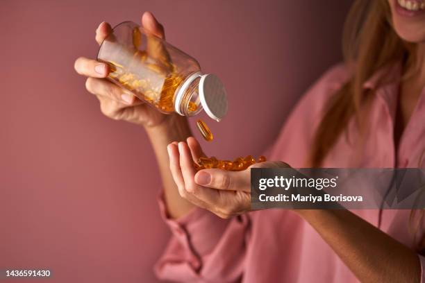 the girl in pink pours omega capsules into her palm. - fish oil stockfoto's en -beelden