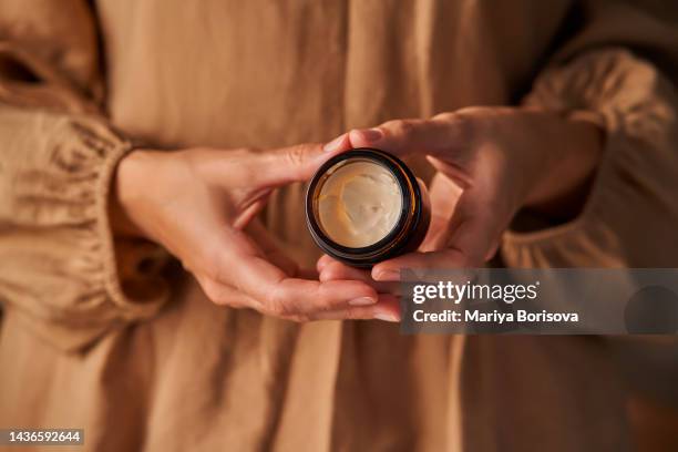 a girl in a beige dress holds an open natural cosmetic cream in her hands. - argan oil stock-fotos und bilder