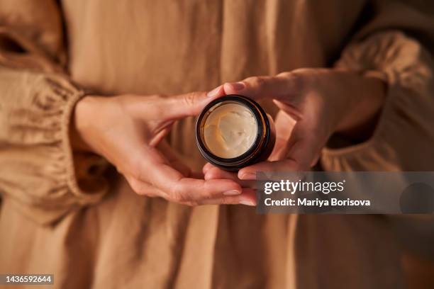 a girl in a beige dress holds an open natural cosmetic cream in her hands. - argan oil stock pictures, royalty-free photos & images
