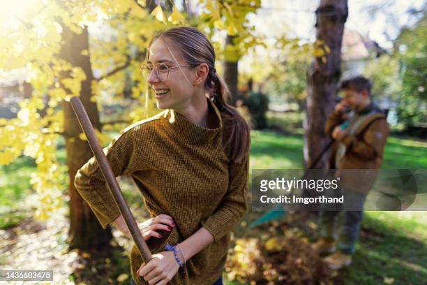 happy teenagers raking autumn leaves - friends clean stock pictures, royalty-free photos & images
