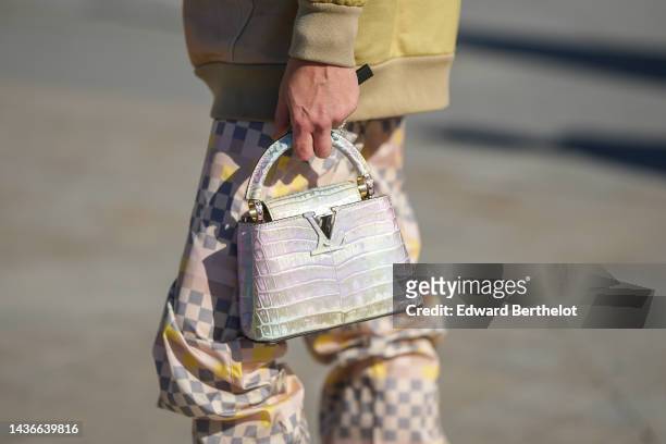 Guest wears a pale yellow bomber coat, pale pink / yellow / gray checkered print pattern flowing silk pants, a pale purple / green shiny leather...