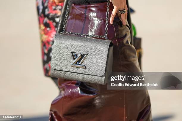 Guest wears a dark brown shiny varnished leather long skirt, a gray Epi leather shoulder bag from Louis Vuitton, rings , outside Louis Vuitton,...