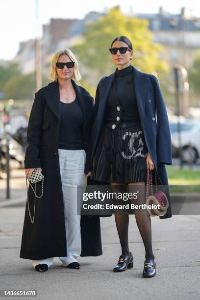 Guest wears black sunglasses, a black t-shirt, a black long wool coat, white large pants, a white pearls shiny clutch from Chanel, black tweed with...