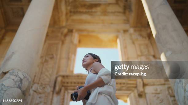 young female tourist taking photos and videos in historical ancient town - beautiful greek women stock pictures, royalty-free photos & images