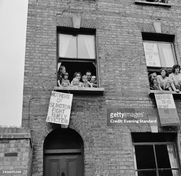 The McDonaugh family with a placard reading 'Mothers of Islington Fight Family Evicton' alongside a window with women with placards reading 'Stop...