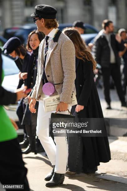 Guest wears a black cap from Chanel, black sunglasses, a black tweed tie, a gold and white pearls necklaces, a white shirt, a white latte and black...