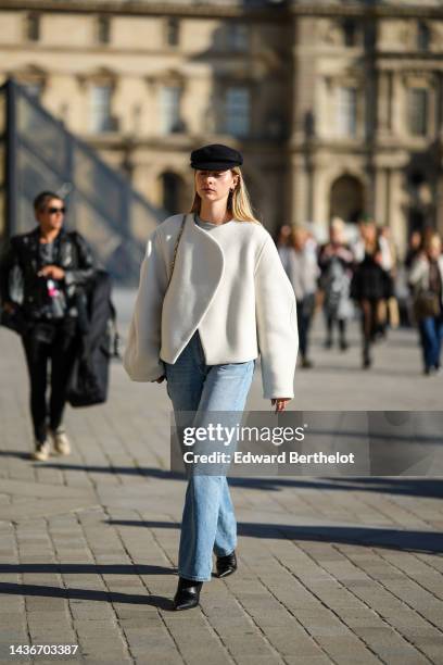 Guest wears black felt wool beret cap, gold earrings, a gray t-shirt, a white wool wrap jacket, a shoulder bag, blue faded denim large pants, black...