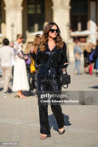 Guest wears black sunglasses, a black sequined shirt from Louis Vuitton, matching black sequined large large pants from Louis Vuitton, a black shiny...