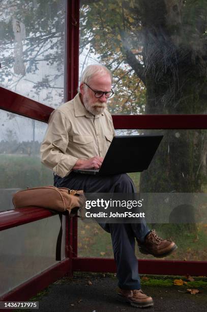 retired man sitting in a bus stop using a laptop - dumfries and galloway stock pictures, royalty-free photos & images