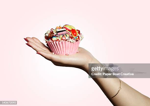 hand holding pink designed cupcake full of sweets - cupcake stock-fotos und bilder