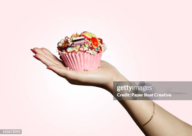 hand holding pink designed cupcake full of sweets - indulged photos et images de collection