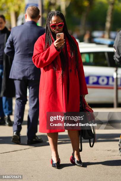 Guest wears red puffy sunglasses from Loewe, a red felt wool long coat, a red midi dress, a red shiny leather and gold nailed / studded City handbag...