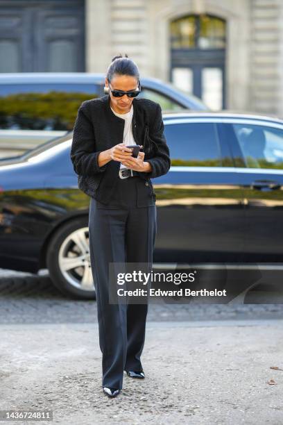 Guest wears black sunglasses, silver large earrings, a white t-shirt, a black tweed jacket from Chanel, a black shiny leather with silver buckle belt...