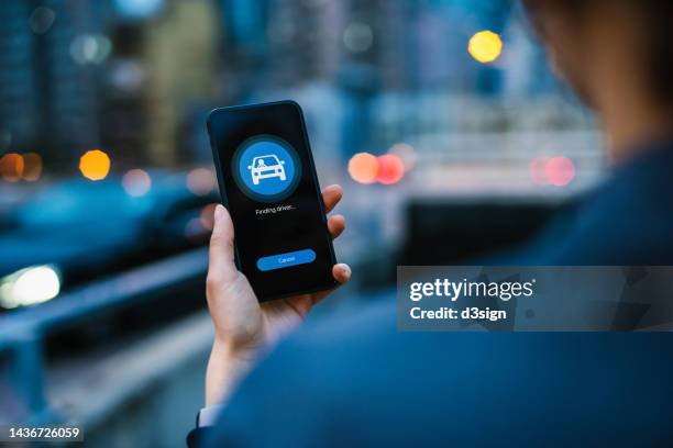 over the shoulder view of young asian woman arranging a taxi service with mobile app on smartphone in city street in the evening, with illuminated city scene in background. lifestyle and transportation technology. convenience and trustworthy car service - uber　ライドシェア ストックフォトと画像