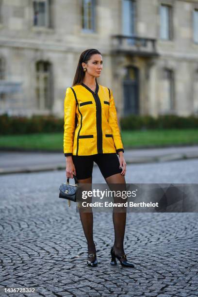 Sabina Jakubowicz wears a black satin headband, black and gold earrings from Chanel, a yellow sequined with black borders jacket, black cyclist...