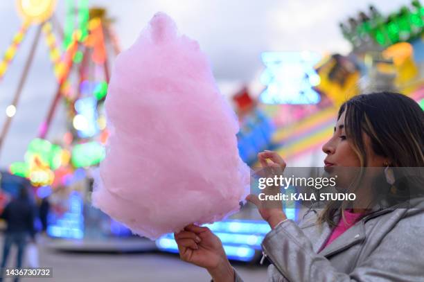 young ethnic lady eating fairy floss in amusement park. young woman with cotton candy in pleasure ground - sugar shack stock-fotos und bilder