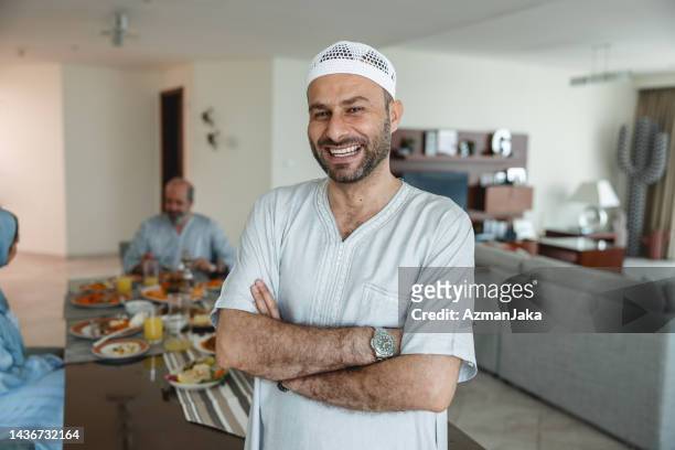 portrait of middle eastern adult male smiling while standing cross-armed in front of dining table - ghoutra stock pictures, royalty-free photos & images