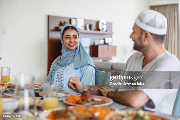 middle eastern couple sitting at dining table full of traditional food - ghoutra stock pictures, royalty-free photos & images