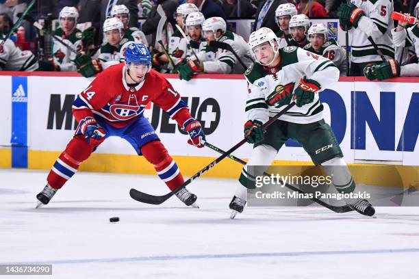 Calen Addison of the Minnesota Wild plays the puck ahead of Nick Suzuki of the Montreal Canadiens during the second period at Centre Bell on October...