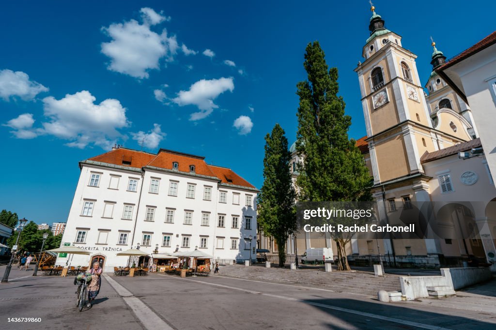 Senior woman walking with her bicycle by Pogačar Square with Ljubljana Cathedral on the right.