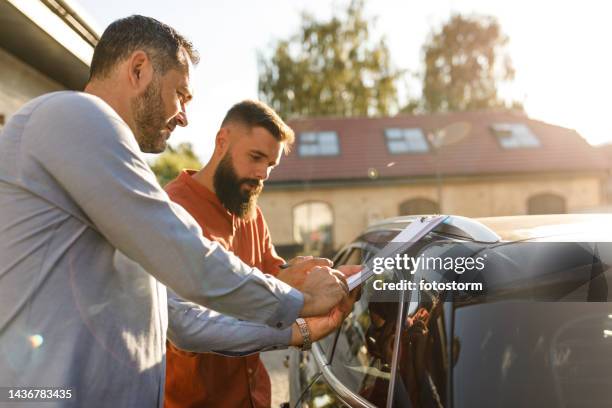 verkäufer gibt seinem kunden ein klemmbrett zum unterschreiben, nachdem er ihm ein auto verkauft hat - used car selling stock-fotos und bilder