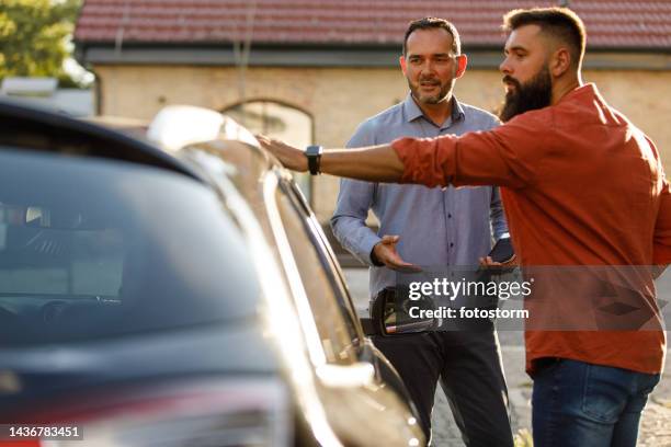 vendedor mostrando un automóvil a un cliente, compartiendo actuaciones mientras inspecciona el vehículo - used car fotografías e imágenes de stock