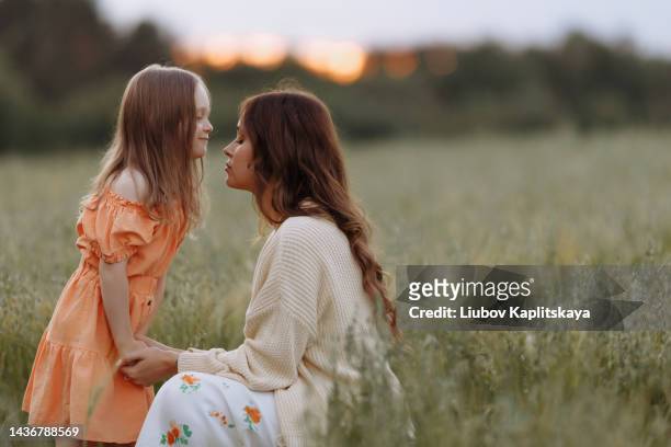 a young mother hugs her daughter 6 years old in a dress sitting on a path in a field with tall grass. - 30 34 years stock-fotos und bilder