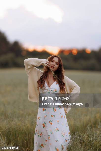 young woman with long hair posing while standing in a wheat field with tall grass. - vestido comprido - fotografias e filmes do acervo