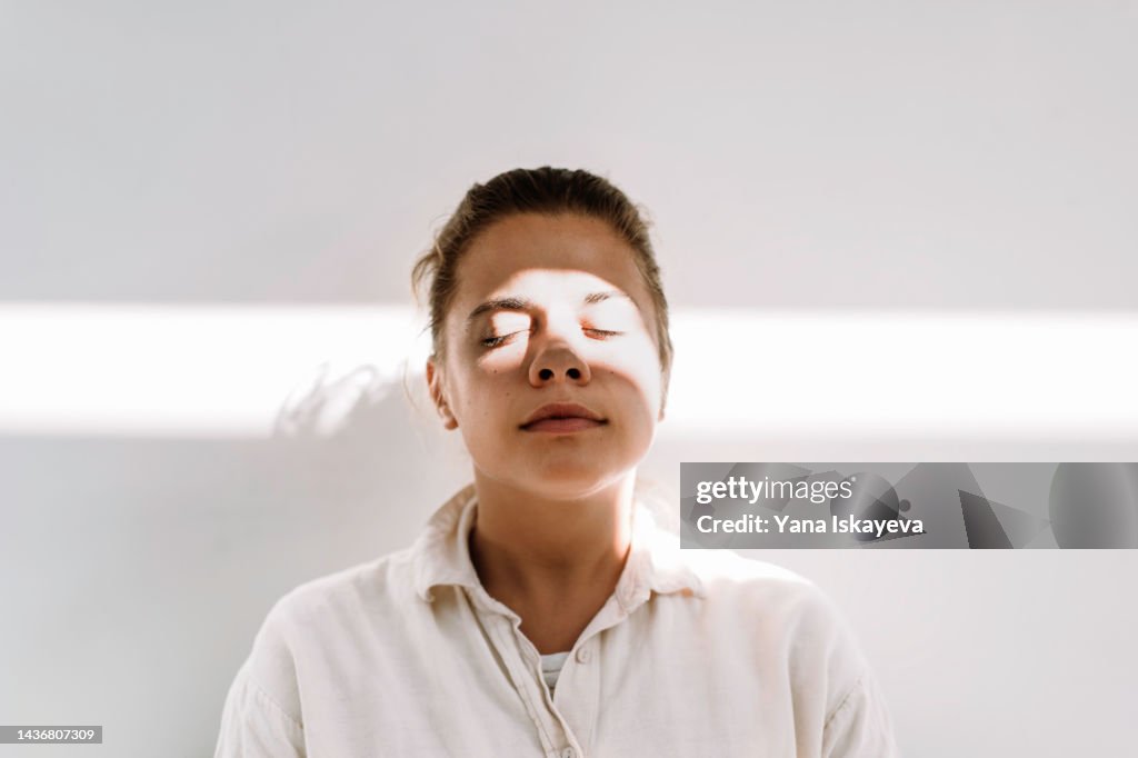 Beautiful tanned woman enjoys the sun against white wall