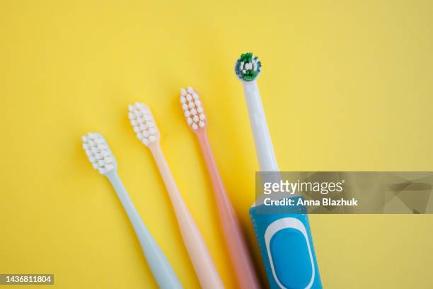 three multi-colored manual toothbrushes and one electric toothbrush over yellow background - electric toothbrush stockfoto's en -beelden
