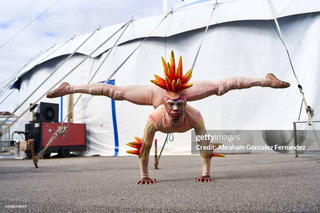 A circus contortionist in a colorful costume practicing his act by balancing with his hands on the ground and his legs stretched in the air.