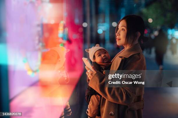 young asian mother using smartphone while doing christmas shopping with her daughter - dezember stock-fotos und bilder
